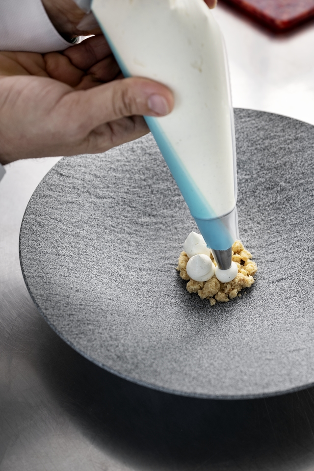Piping cream onto a crumble base in a serving bowl