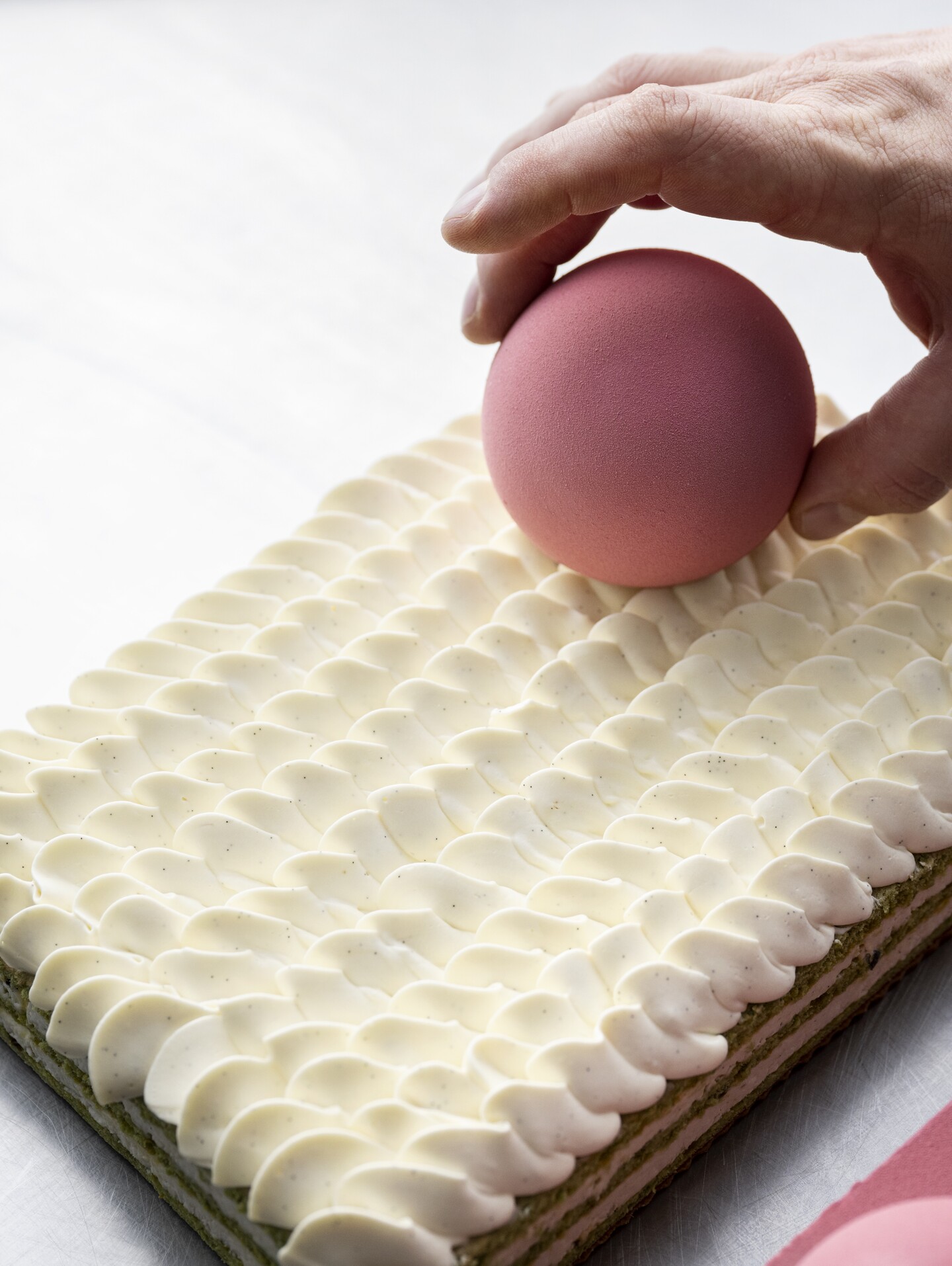 Main plaçant une sphère rose sur un gâteau