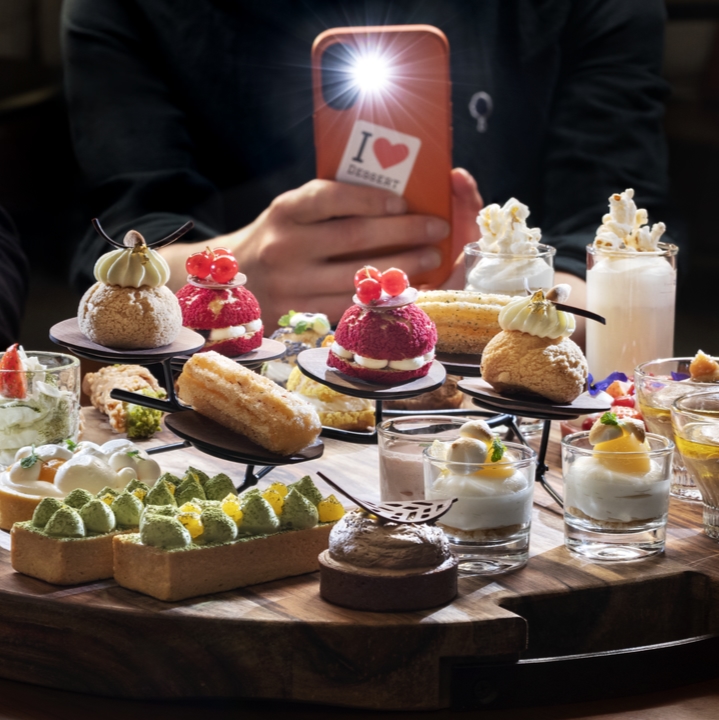 Goście fotografujący asortyment deserów finger-food ułożonych na dużej tacy.