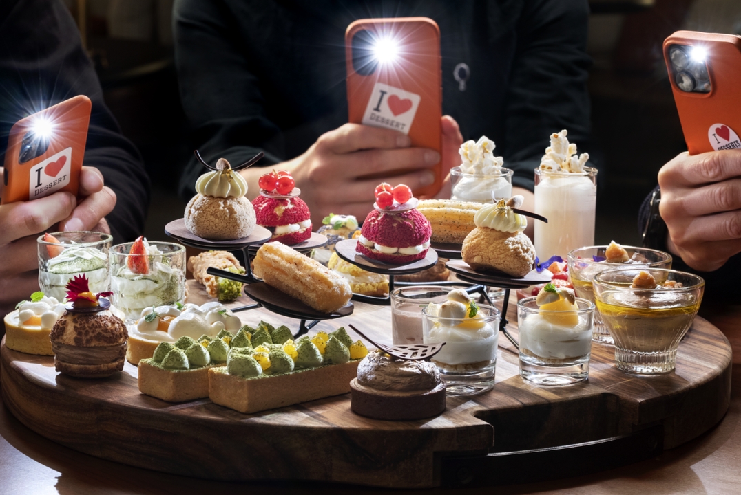 Goście fotografujący asortyment deserów finger-food ułożonych na dużej tacy.