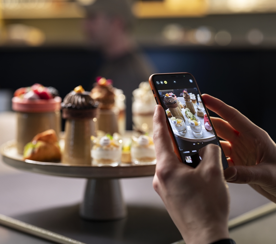 Person photographing a tray of assorted dessert tapas on a phone.