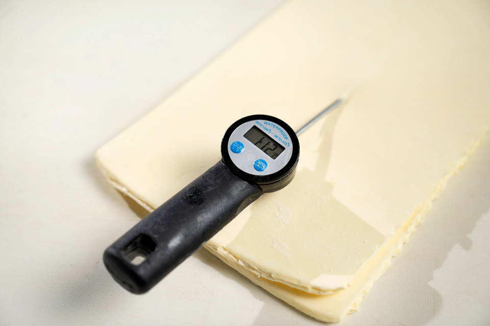 Digital thermometer placed on a sheet of laminated dough.