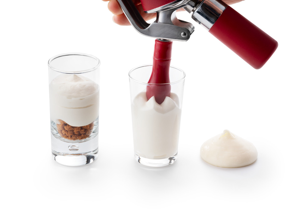 Three applications of Debic Cheesecake on a white background: a light cheesecake mousse layered over crumble in a glass, cheesecake espuma being dispensed into a glass from a siphon, and a dollop of crème chibouste.