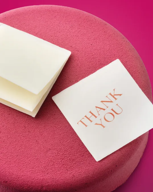 Pink cake with white chocolate squares and a note topper.