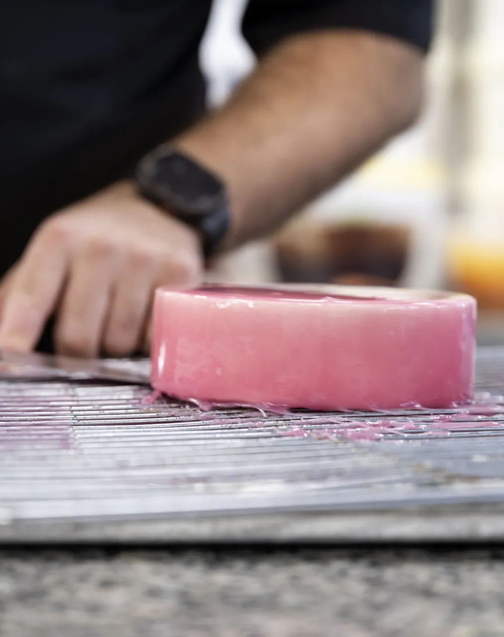Pink glazed cake being trimmed on a cooling rack
